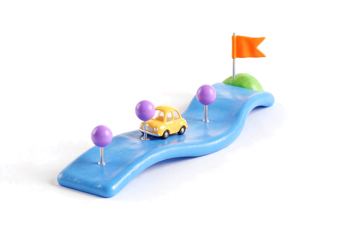 Winding blue road with three purple waypoints, yellow car and orange flag